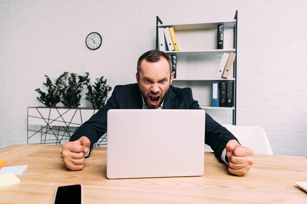 Portret van overwerkte zakenman in pak gillend op de werkplek met laptop in kantoor - Foto, afbeelding