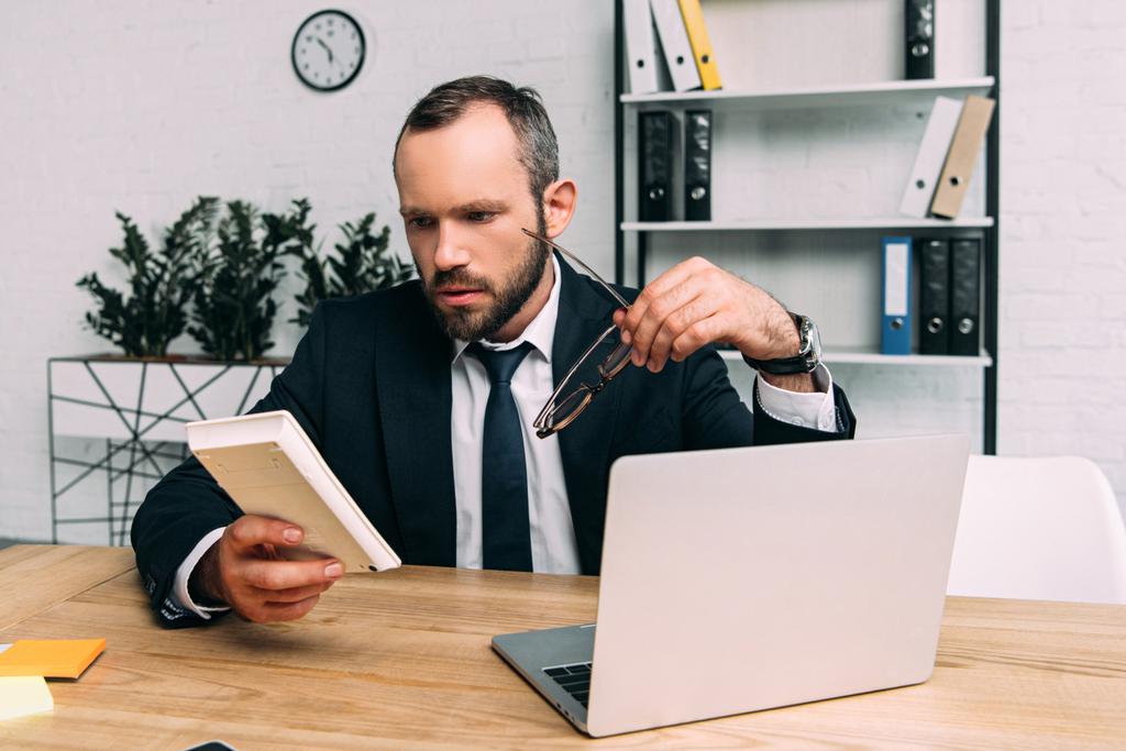 homme d'affaires concentré avec calculatrice et lunettes sur le lieu de travail avec ordinateur portable au bureau
 - Photo, image