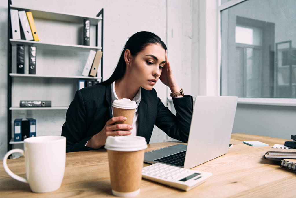 уставшая деловая женщина в костюме с кофе идти работать на ноутбук на рабочем месте в офисе
 - Фото, изображение