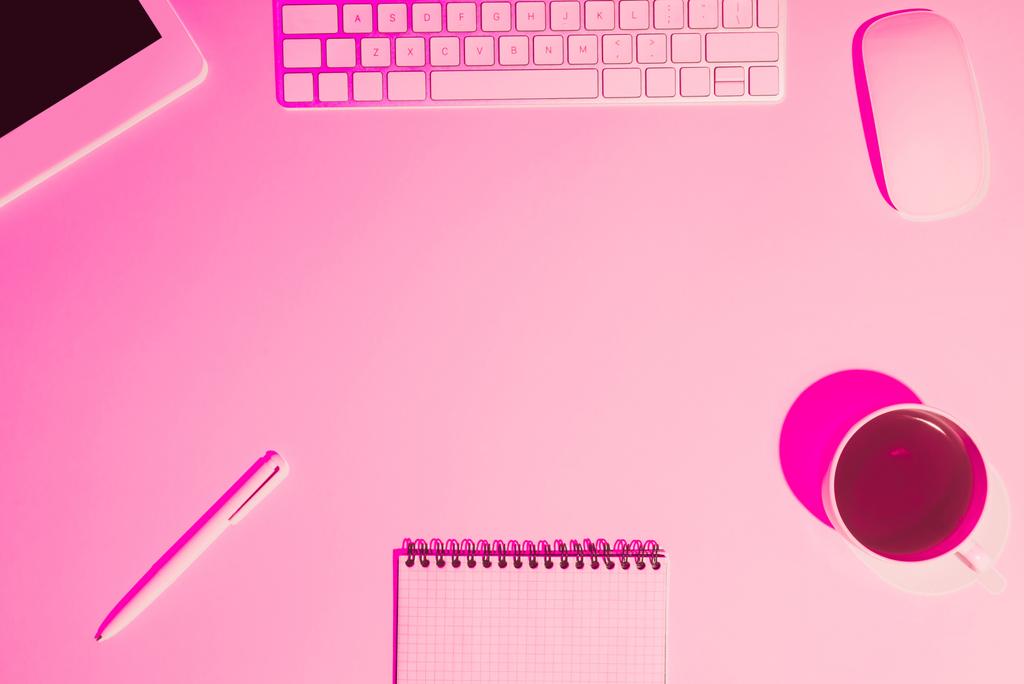 rosa getöntes Bild von Kaffeetasse, digitalem Tablet, Stift, Lehrbuch und Computertastatur auf dem Tisch  - Foto, Bild