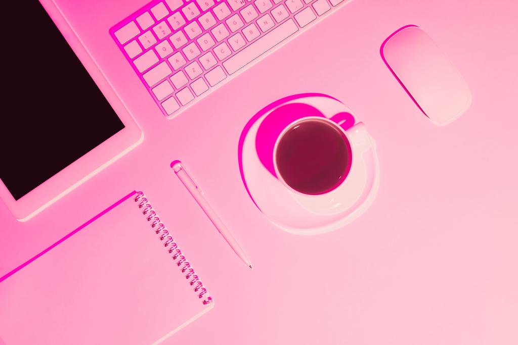 コーヒー カップ、デジタル タブレット、ペン、教科書、コンピューターのキーボードとマウス テーブルの上のピンクのトーンの画像  - 写真・画像