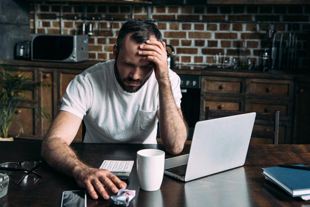 deprese mladý muž sedí na kuchyň s notebookem a zmačkaný fotografie ex přítelkyně - Fotografie, Obrázek