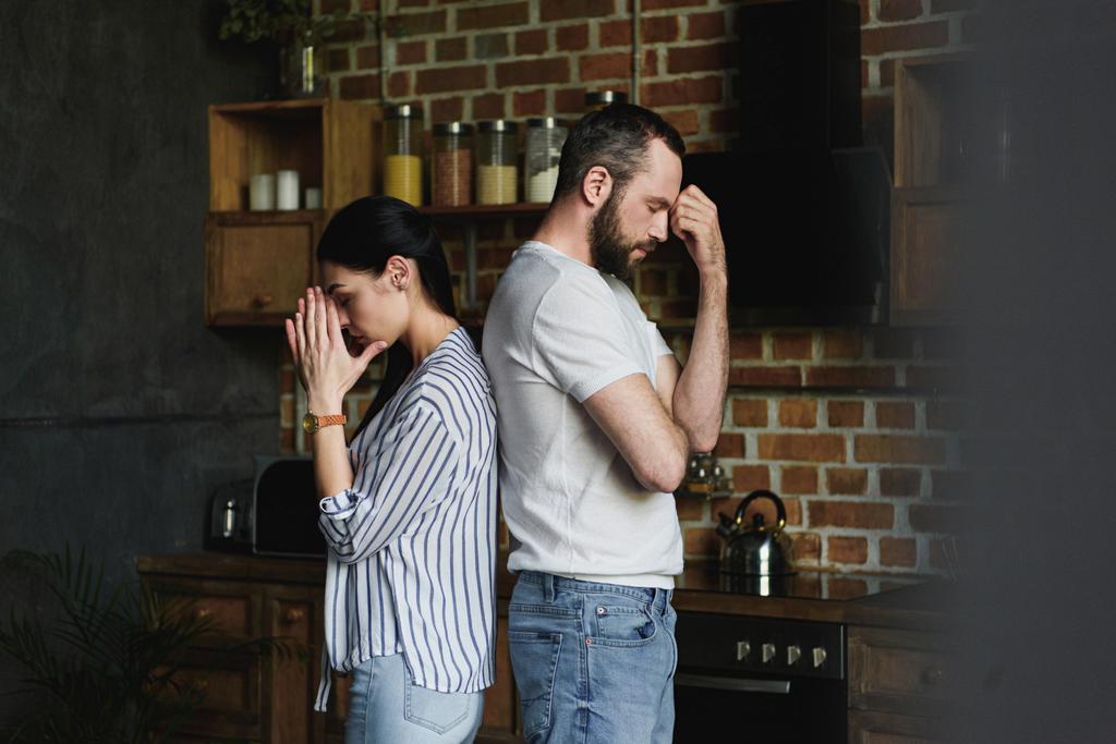 Zijaanzicht van jonge depressief paar staande rug aan rug na ruzie thuis - Foto, afbeelding