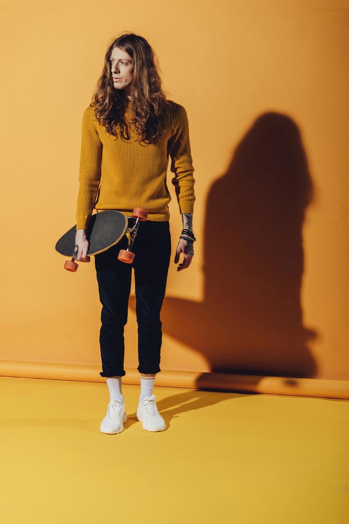 elegante stijlvolle man poseren met skateboard, op geel - Foto, afbeelding