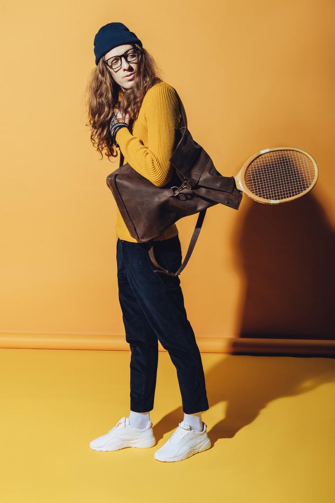 knappe man met vintage rugzak en houten tennisracket, op geel - Foto, afbeelding