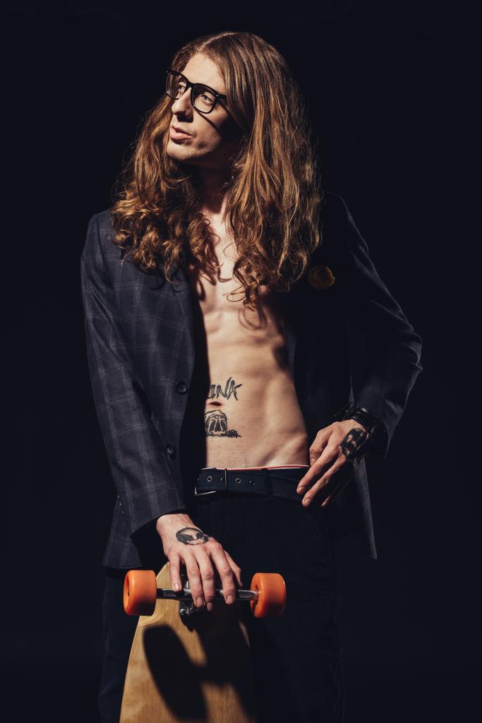 modieuze getatoeëerd skateboarder poseren geïsoleerd op zwart - Foto, afbeelding