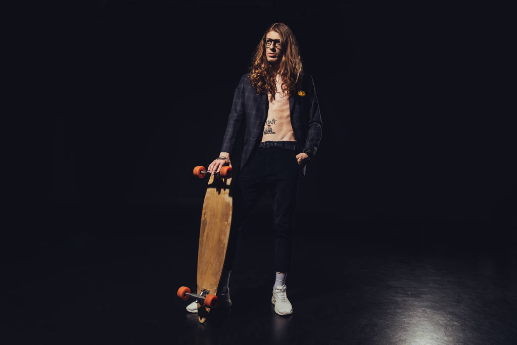 Módní pohledný muž pózuje s skateboard na černém pozadí - Fotografie, Obrázek