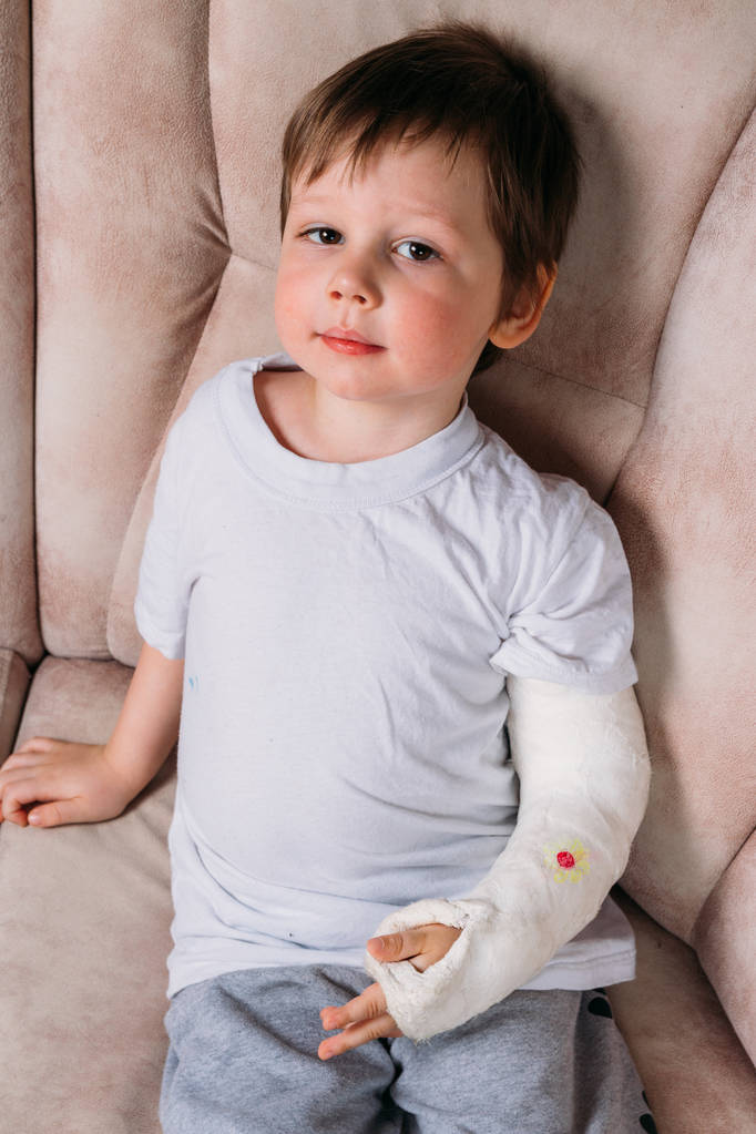 un niño pequeño está sentado en una silla con un brazo roto, en un yeso. hospital. medicina. peligro. dolor. para romper extremidades. violencia
. - Foto, Imagen