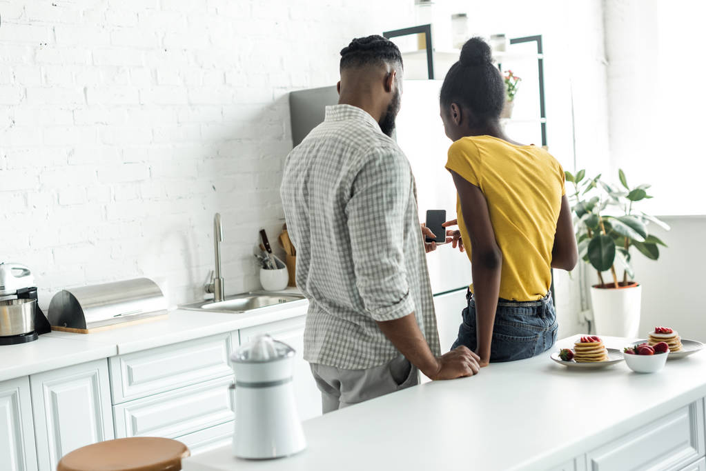 Widok z african american para patrząc na smartfon w kuchni tyłu - Zdjęcie, obraz