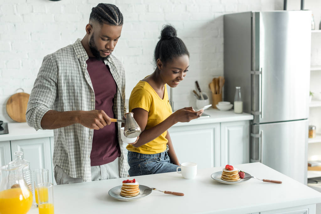 アフリカ系アメリカ人のガール フレンドは、キッチンでスマート フォンを持つパンケーキの写真を撮影 - 写真・画像