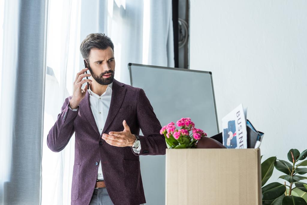 ontslagen jonge zakenman praten via de telefoon in de buurt van vak van persoonlijke spullen op kantoor - Foto, afbeelding