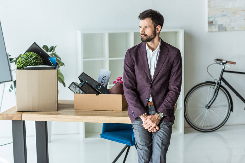 promyšlené mladý podnikatel s krabice osobních věcí, opřel se o stůl v kanceláři - Fotografie, Obrázek
