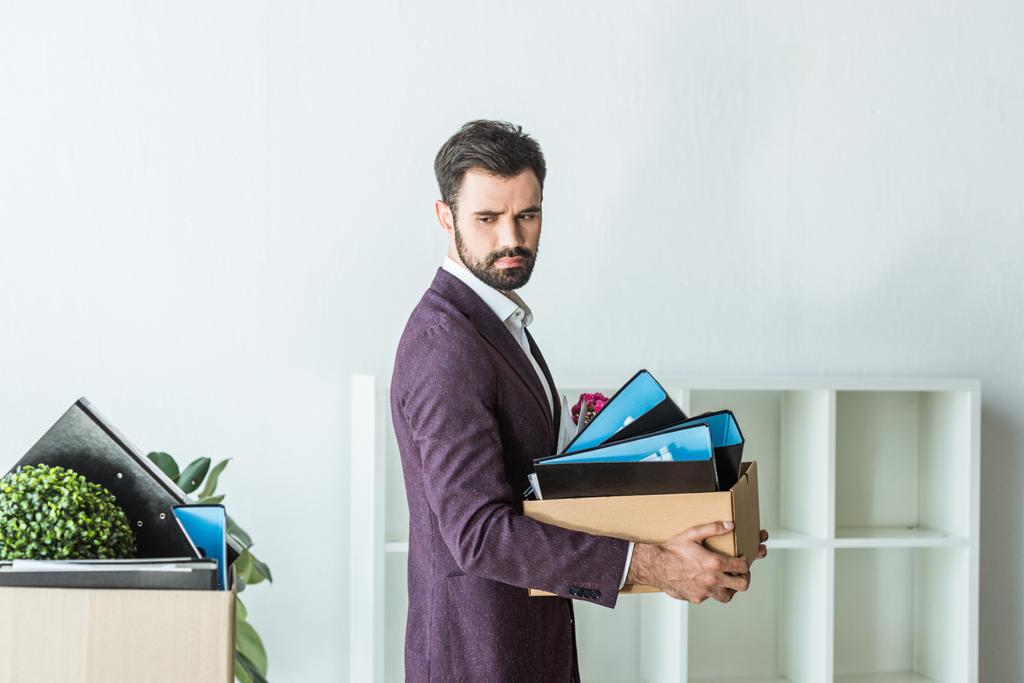 side view of fired young businessman carrying box of personal stuff at office - Photo, Image
