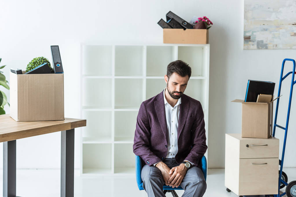 hombre de negocios despedido deprimido sentado en la silla en la oficina con cajas de cosas personales
 - Foto, Imagen