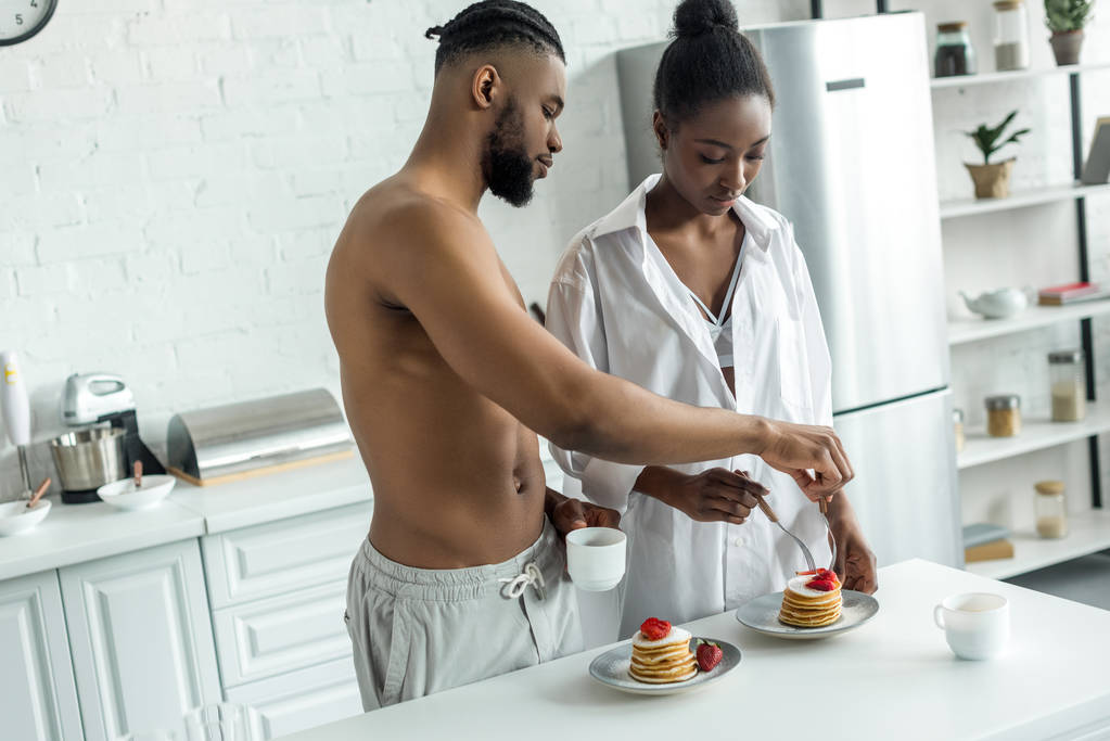 キッチンで朝食にパンケーキを食べるアフリカ系アメリカ人のカップル - 写真・画像