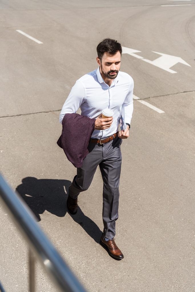 hoge hoekmening van knappe jonge zakenman met papieren kopje koffie draaien voor werk - Foto, afbeelding