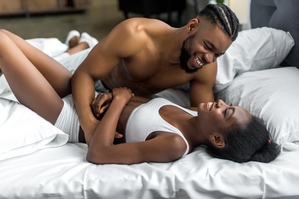 Αφρικανική αμερικανική ζευγάρι χαμογελώντας και Αγκαλιάζοντας στο κρεβάτι στην κρεβατοκάμαρα - Φωτογραφία, εικόνα