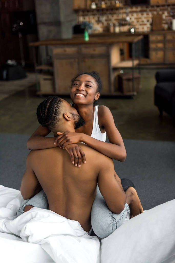 Вид сзади на африканского бойфренда, целующего подругу в спальне
 - Фото, изображение