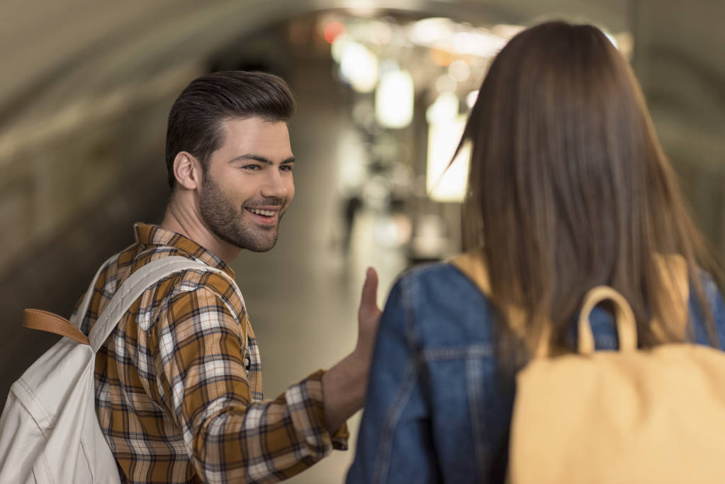 uśmiechnięty mężczyzna turystycznych z plecaka, podając rękę do dziewczyny na stacji metra  - Zdjęcie, obraz