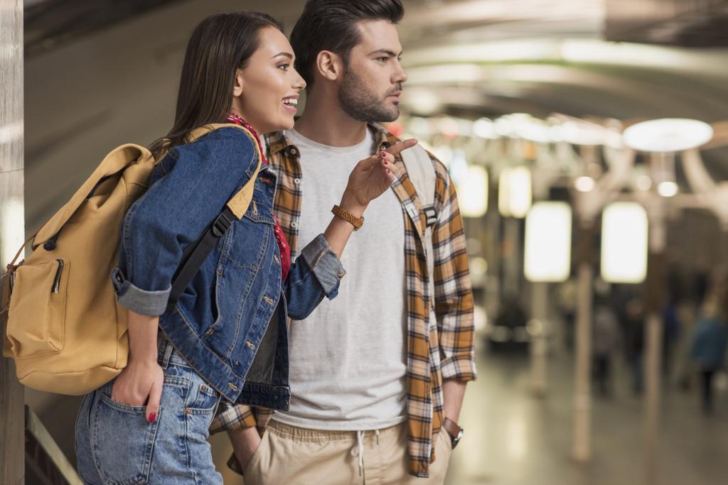 uśmiechający się kobieta dla podróżujących z plecakiem, wskazując palcem na chłopaka na stacji metra  - Zdjęcie, obraz