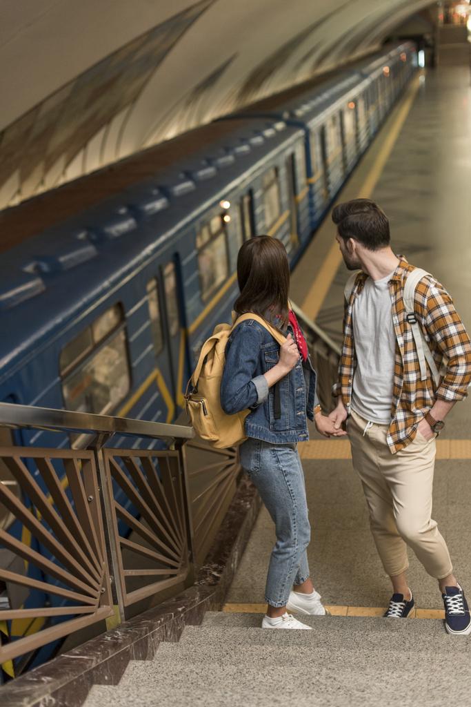 stijlvolle reizigers met rugzakken staande op de trap bij metrostation  - Foto, afbeelding