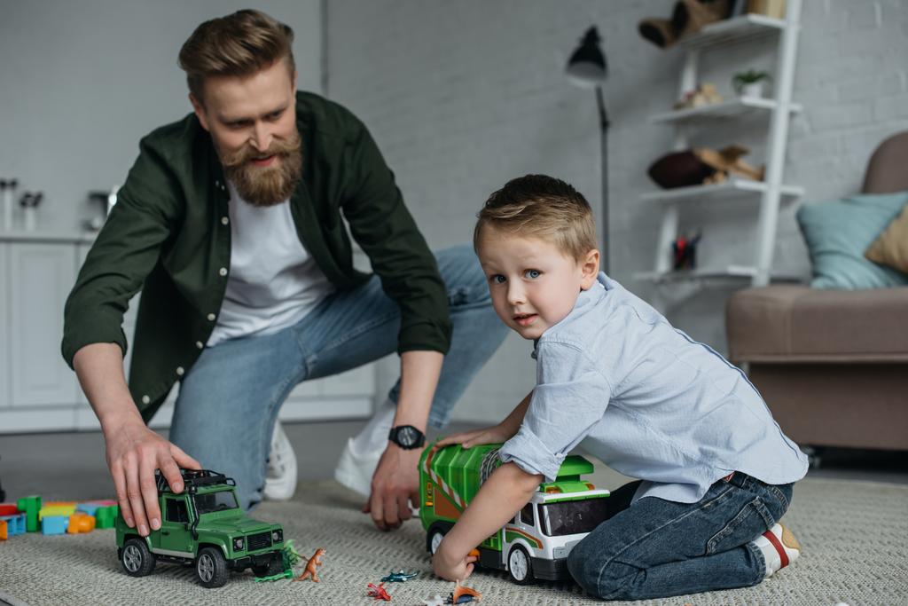 father and little son playing with toy cars together on floor at home - Photo, Image