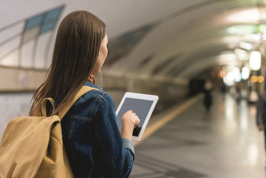 Widok z tyłu stylowe kobiety z cyfrowego tabletu i słuchawki w stacji metra  - Zdjęcie, obraz
