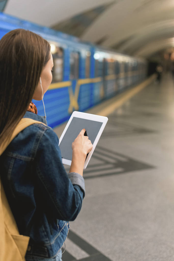 πίσω όψη του κομψή γυναίκα με ακουστικά και ψηφιακή δισκίο στο σταθμό του μετρό  - Φωτογραφία, εικόνα