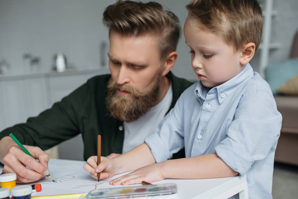 батько і милий маленький син з барвистими олівцями малюють фотографії разом вдома
 - Фото, зображення