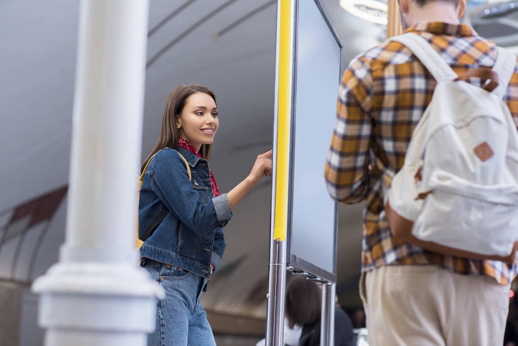 Widok z tyłu mężczyzna turysty z plecaka i jego dziewczyna, patrząc na tablicy informacyjnej na stacji metra  - Zdjęcie, obraz