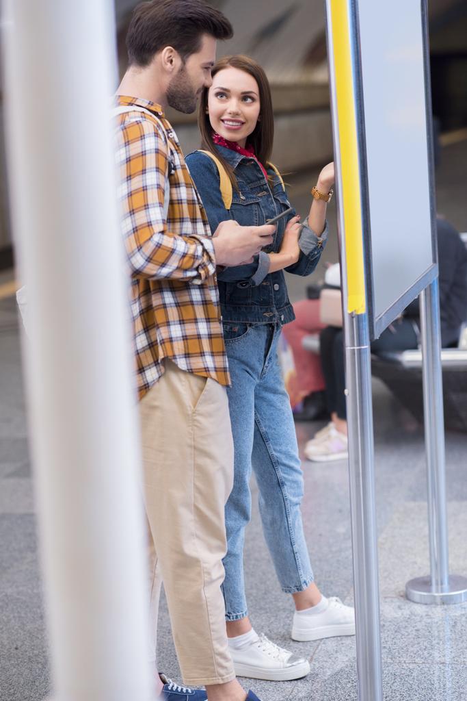 Seitenansicht von stilvollen Touristen, die an der U-Bahn-Station eine Informationstafel betrachten  - Foto, Bild