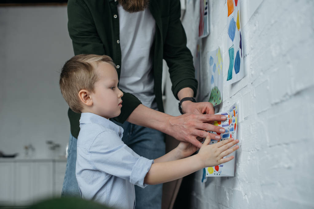 Teilansicht einer Familie, die zu Hause kindische Zeichnung an Wand hängt - Foto, Bild