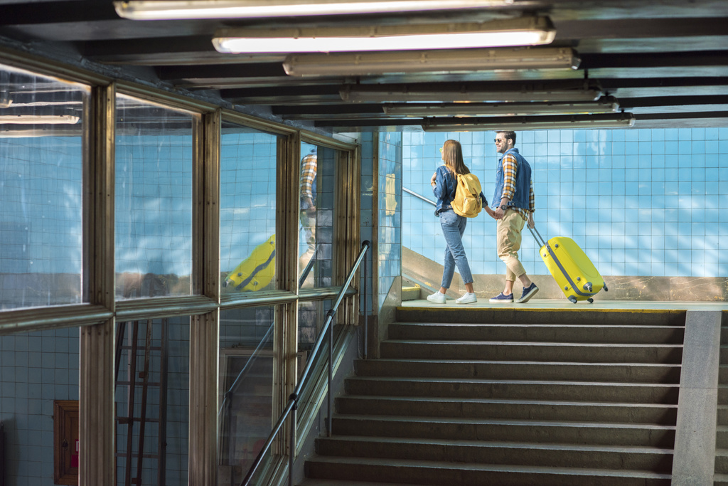 κομψό ζευγάρι με σακίδιο και τροχοφόρα τσάντα πάει επάνω στο μετρό  - Φωτογραφία, εικόνα