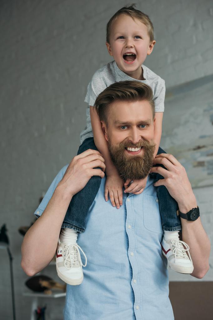 mosolygó apa és kisfia, vállán szórakozás otthon ül - Fotó, kép