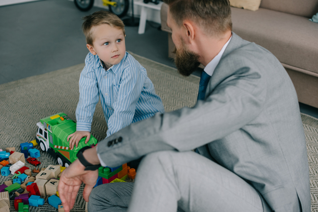 liikemies puku ja pieni poika leikkii värikkäitä lohkoja yhdessä lattialla kotona, työn ja elämän tasapaino käsite
 - Valokuva, kuva