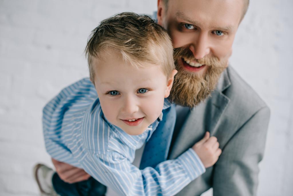 Porträt eines lächelnden Geschäftsmannes im Anzug und eines kleinen Sohnes, die sich umarmen - Foto, Bild
