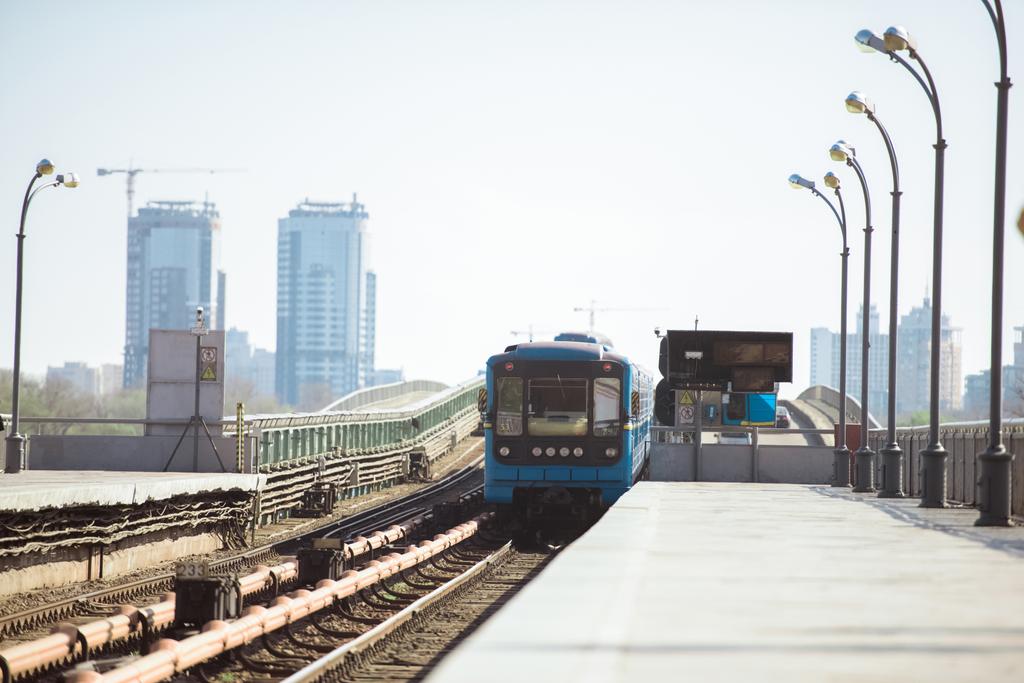 прибуття поїзда на відкритій станції метро з будівлями на фоні
 - Фото, зображення