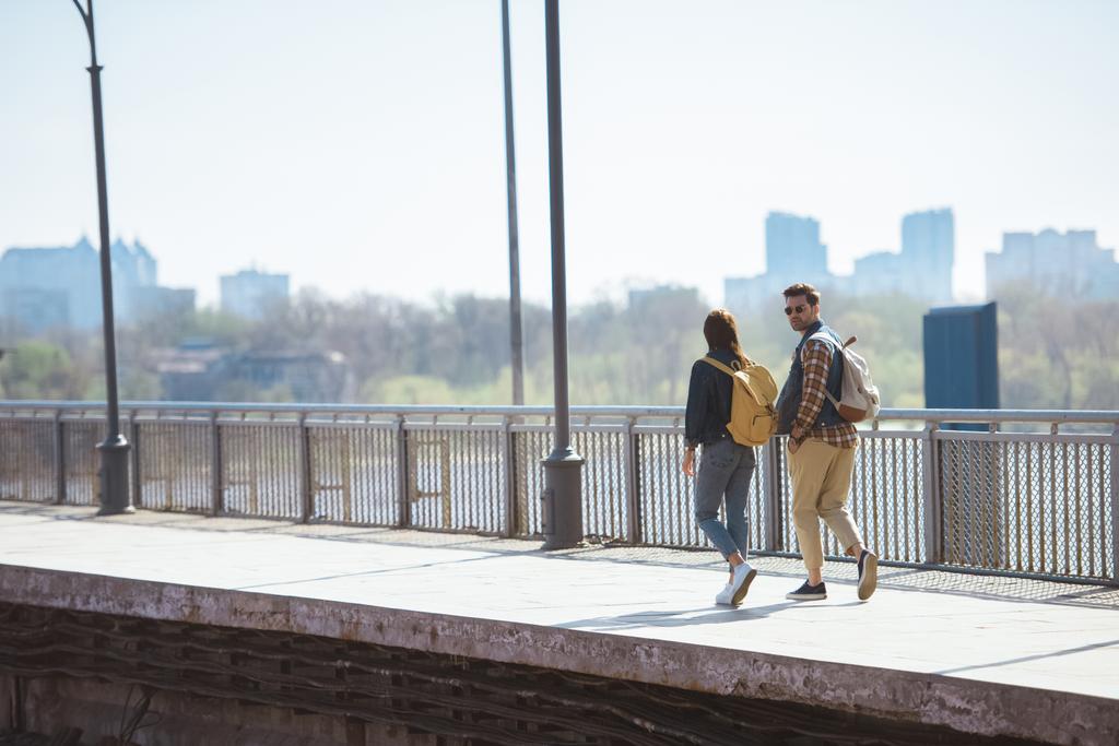 vista distante do casal de turistas elegantes com mochilas indo na estação de metrô ao ar livre
 - Foto, Imagem