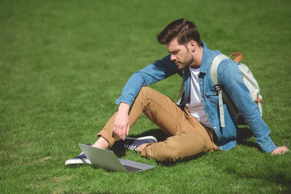 ラップトップと草の上に座っている若い男  - 写真・画像