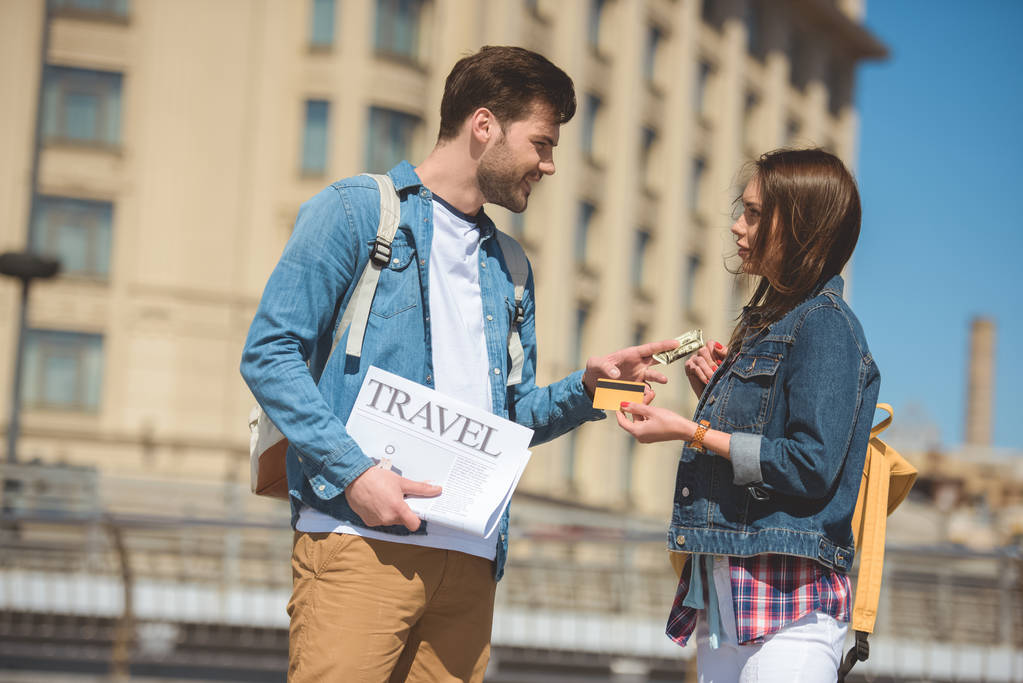 mužské turistické cestování noviny dávat bankovky dolaru přítelkyni kreditní kartou v ruce - Fotografie, Obrázek