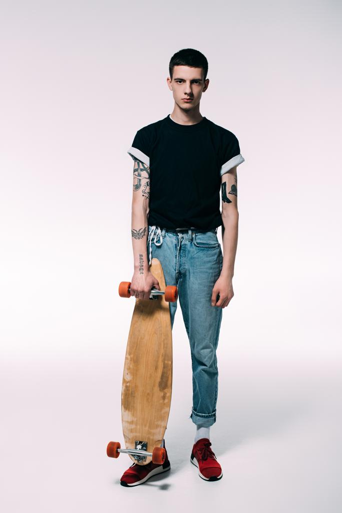 Tipo con brazos tatuados sosteniendo longboard sobre fondo blanco
 - Foto, Imagen