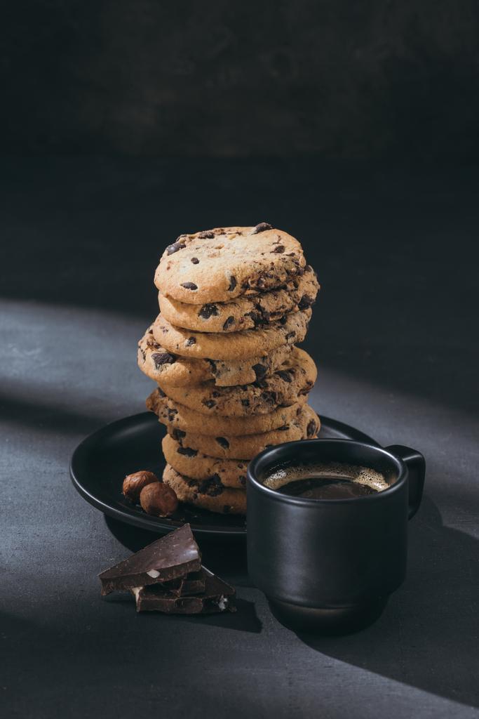 pila de galletas de chispas de chocolate en el plato con taza de café en la superficie negra
 - Foto, imagen