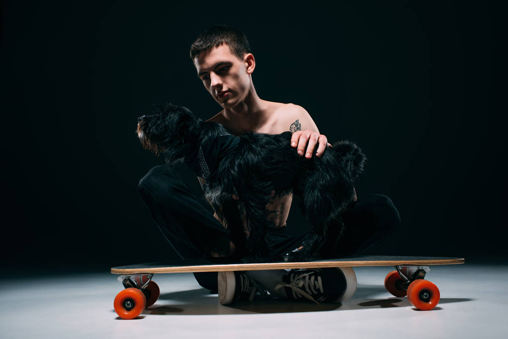 Schwarzer Hund steht auf Longboard seines Besitzers auf dunklem Hintergrund - Foto, Bild