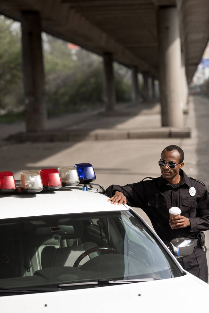 poliisi, jolla on kahvia mennä nojaamaan poliisiautoon kadulla
 - Valokuva, kuva