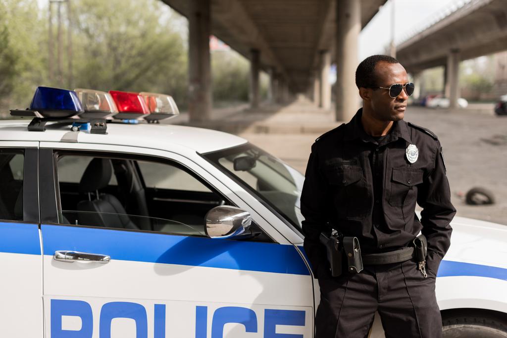 policial afro-americano apoiando-se de volta no carro e olhando para longe
 - Foto, Imagem