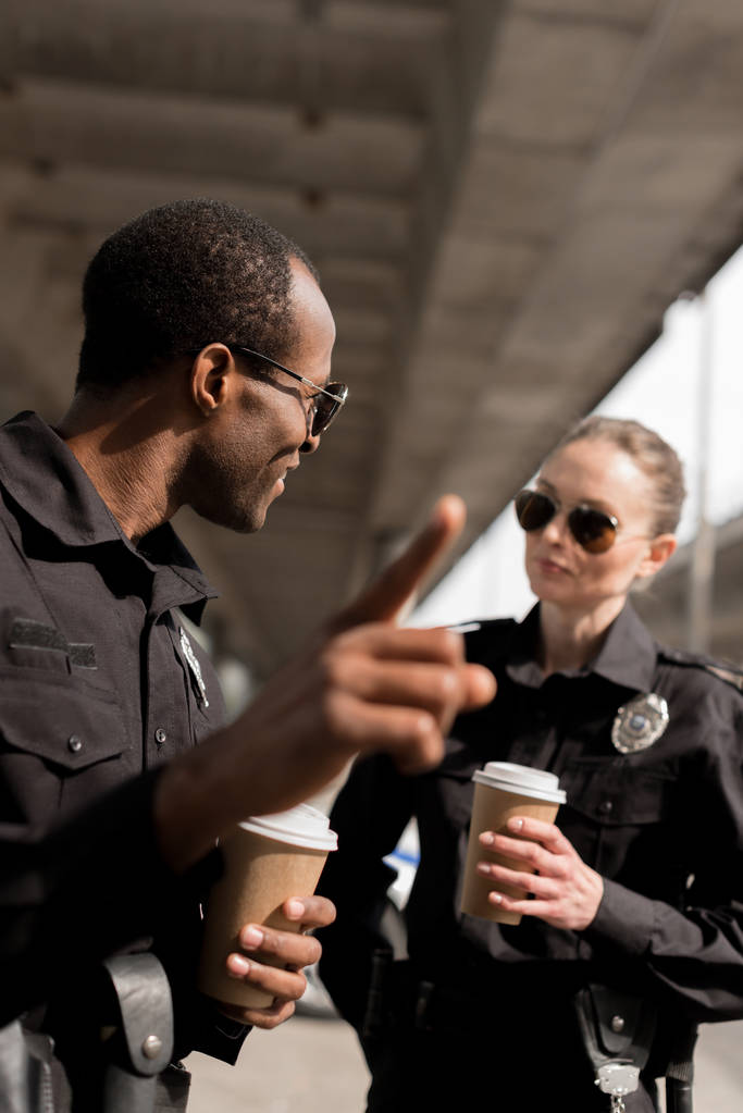 politieagent ergens te wijzen terwijl het drinken van koffie om te gaan met partner - Foto, afbeelding