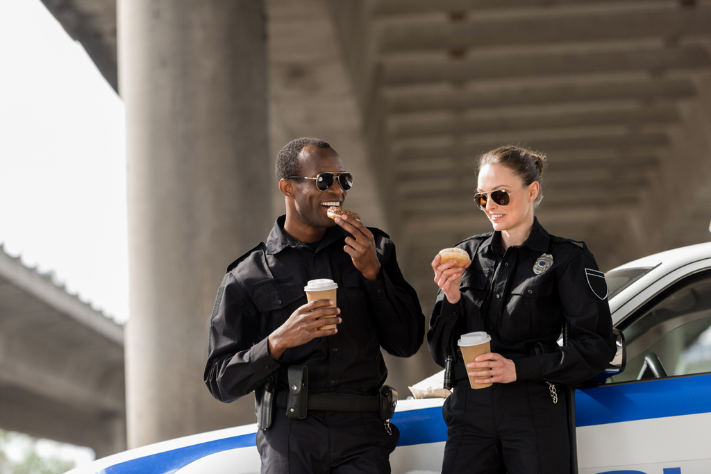 jovens policiais com café e donuts de pé ao lado do carro sob ponte
 - Foto, Imagem