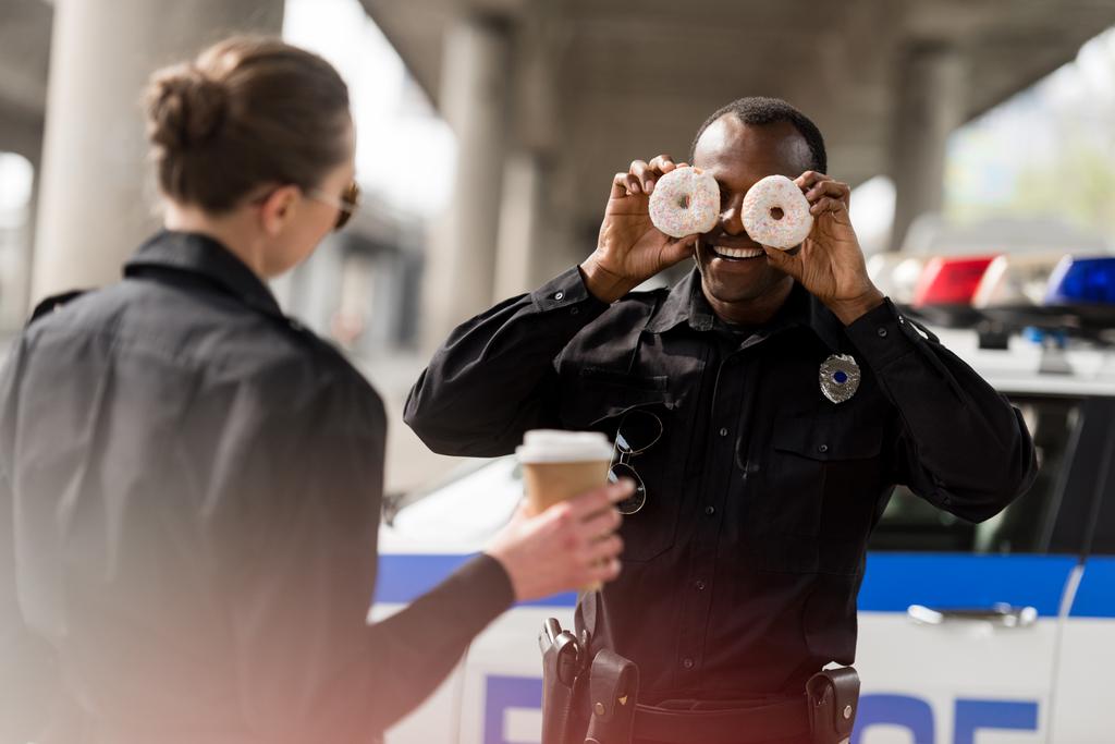 policial afro-americano fingindo donuts como seus olhos para divertir seu parceiro
 - Foto, Imagem