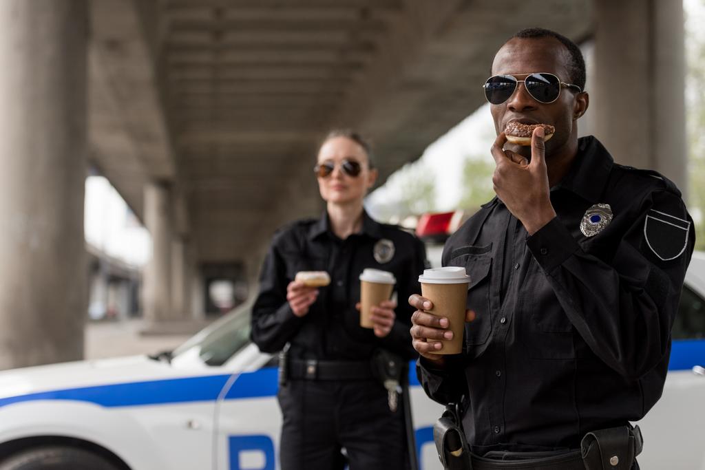 young police officers having coffee break with doughnuts in front of police car - Photo, Image