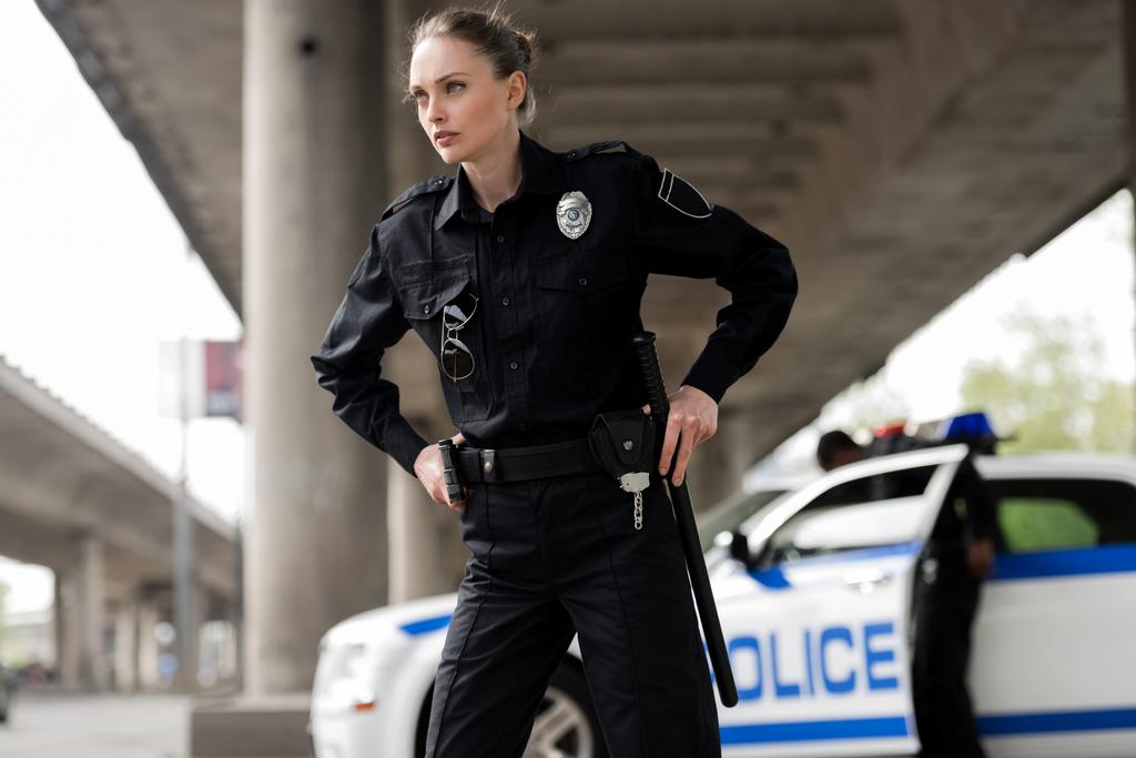 уверенная женщина-полицейский смотрит в сторону и вынимает пистолет и биту
 - Фото, изображение